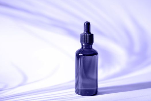 Serum bottle on purple background with palm leaf shadow. Color of the year 2022 Very Peri