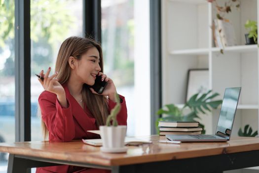 Young asian freelancer business woman working online via internet at home. Using mobile phone call with customer