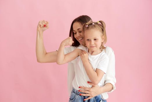 Funny family on the background of a bright pink wall. Mother and her daughter little girl having fun, showing that the strength of the muscles. Woman power, feminism.