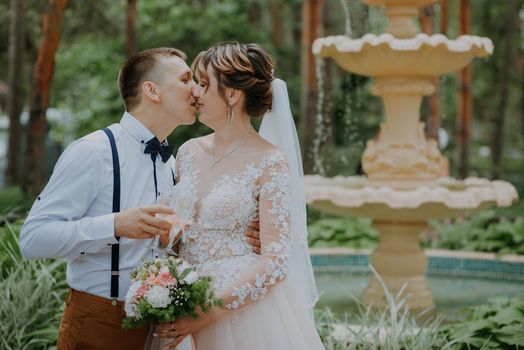 Kiss of the groom and the bride holding glasses with champagne