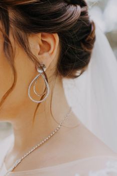 beautiful earring with diamonds in the ear of the bride. bride's ear with earring, neck and veil. Beautiful wedding earrings with pearls on the ear, close-up of the bride. Close-up of the bride's neck and chest, framed in white wedding lace and with an elegant earring in her ear