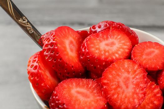 Detail on strawberries cut in circles, in white ceramic bowl with silver spoon.