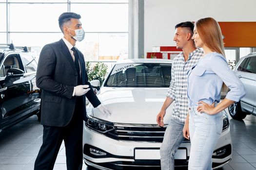 Man car salesman in face mask talking to a client in car showroom