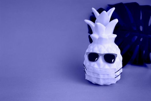 Pineapple in a medical mask and sunglasses on very peri background. Summer concept. Vision for the summer of 2022 during the coronavirus pandemic. Demonstrating the colors of 2022 - Very Peri.