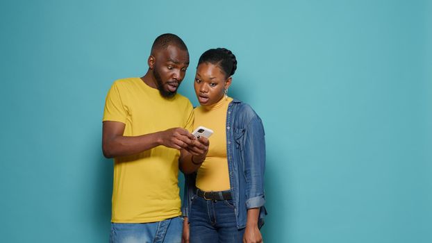 Man and woman using internet on smartphone together in front of camera. People looking at mobile phone display and having positive connection. Modern couple working with technology.