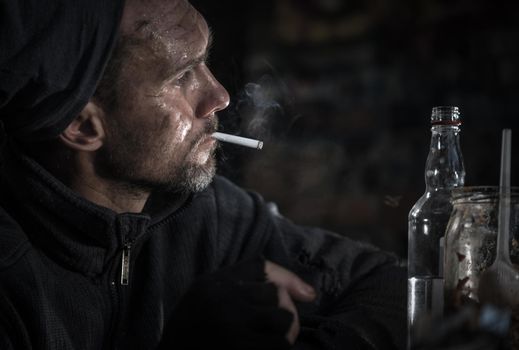 Dirty Caucasian Homeless Men in His 40s with Cigarette and Bottle of Vodka. Social Issues Theme.