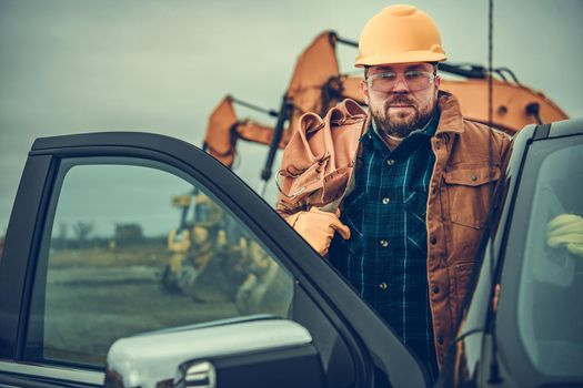 Caucasian Construction Contractor Worker in His 30s with Tool Belt on His Shoulder Staying Next to His Truck.