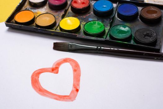 Kid painting heart shape with brush during coronavirus quarantine at home.