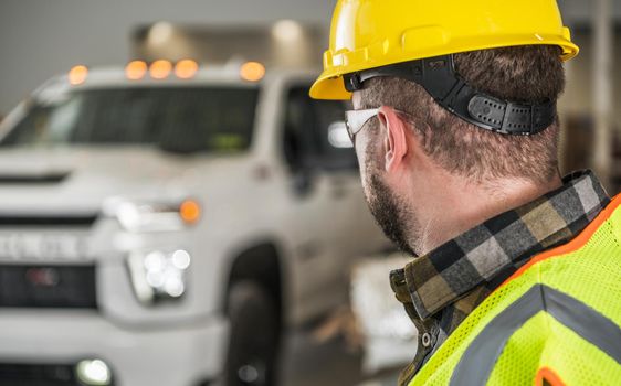 Construction Worker in Yellow Hard Hat and Eyes Protection Glasses Looking at His Brand New Commercial Pickup Truck