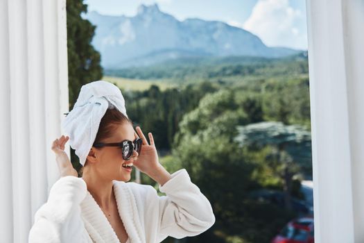 Portrait of gorgeous woman in a white robe on the balcony bit on green nature Perfect sunny morning. High quality photo