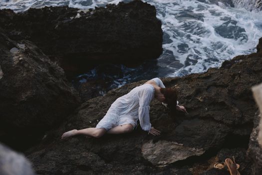 Beautiful bride in long white dress wet hair lying on a rocky cliff view from above. High quality photo