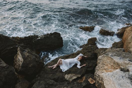 Beautiful bride lying on rocky coast with cracks on rocky surface unaltered. High quality photo