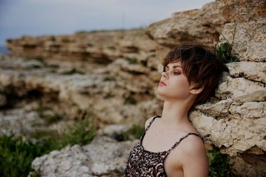 woman in dress short haircut posing sitting on the rocks outdoors. High quality photo