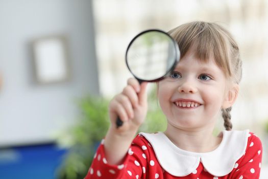 Portrait of pretty little child hold magnifying glass and explore world through it. Smiling happy kid investigate items. Vision, explore, childhood concept