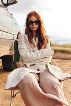 woman sitting on a chair in a field wearing dark glasses near the car endless field. High quality photo