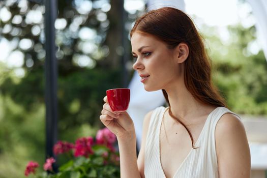 Young stylish woman in a white dress drinks coffee outdoors in a cafe unaltered. High quality photo