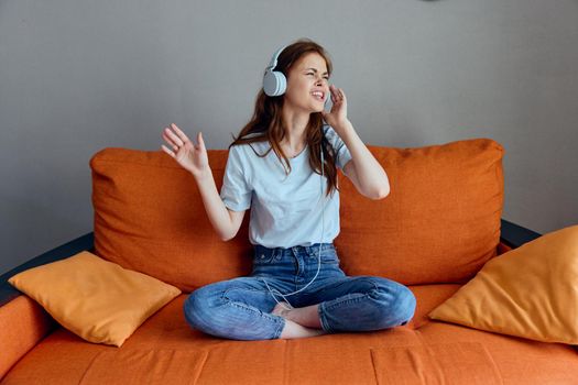 pretty woman listening to music with headphones on the orange sofa apartments. High quality photo