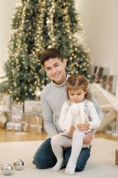Happy young boy with his niece play in front of fir tree. Christmas mood.