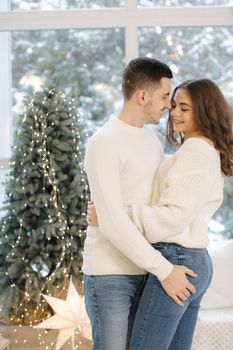 Beautiful young couple posing to photographer at New Year studio. Christmas tree. Snow outside.