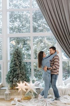 Handsome man with his gorgeous five stand in front of big window. Snow outside. Fir tree and lot of presents for Christmas fairy tail.