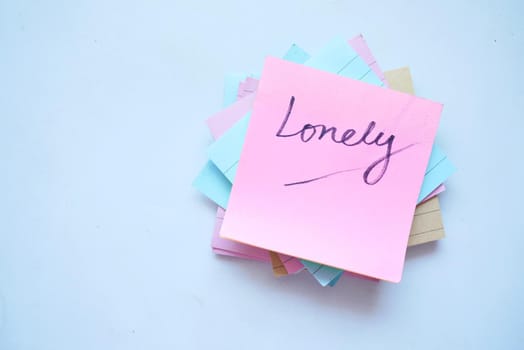hand written lonely text on a sticky note on white background .