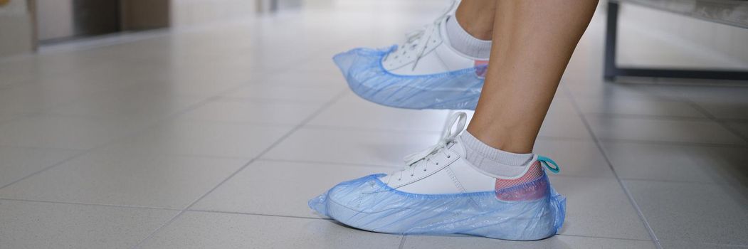 Women legs in sneakers with shoe covers in hospital corridor. Disposable shoe covers for visiting medical institutions concept