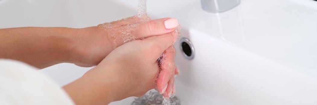 Woman washes hands under running water in sink. Hand hygiene concept