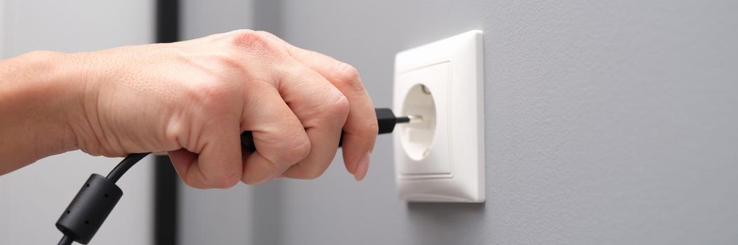 Woman hand inserts an electrical plug into outlet. Energy saving concept