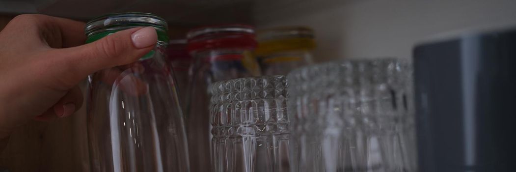 Woman hand pulls out glass cup from cabinet in kitchen. Set of glass glasses concept