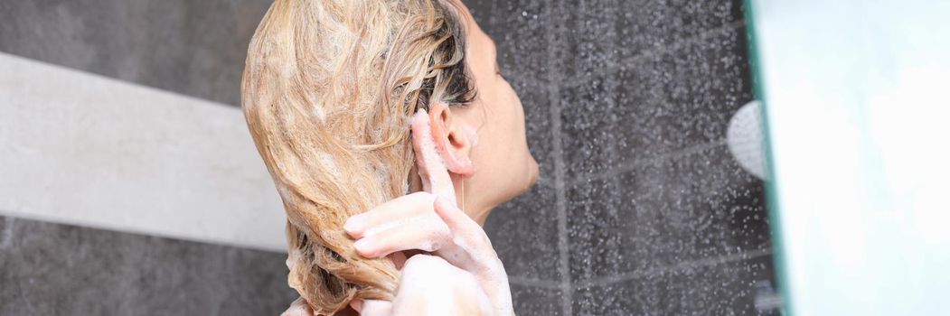 Young woman washes hair with shampoo in shower. Hair care rules concept