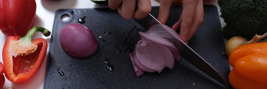 Woman chef cuts red onion on wooden board lie vegetables around. Cooking delicious and healthy vegetarian food concept