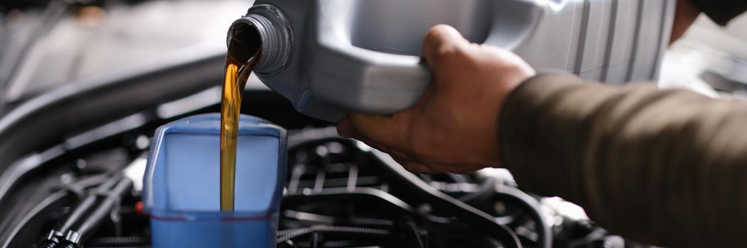 Locksmith mechanic pours engine oil into plastic container on motor engine. Oil change in car engine concept