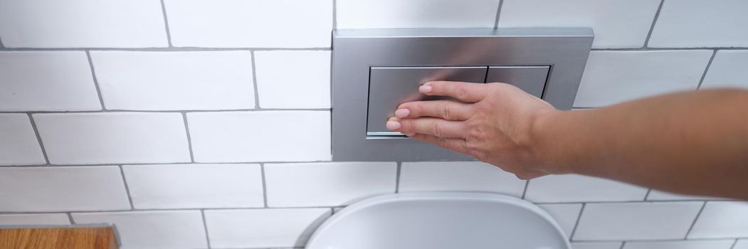 Female hand presses flush button in toilet. Flush cistern button concept