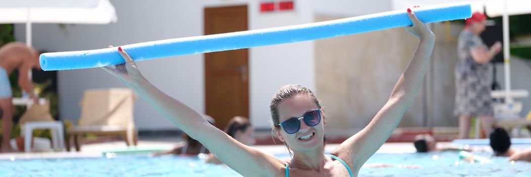 Young woman in sunglasses is engaged in aqua aerobics in outdoor pool. Health benefits of sports in pool concept