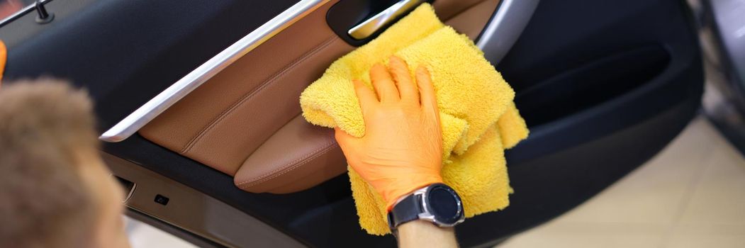 Male washer in gloves wipes car door with microfiber. Car wash services concept