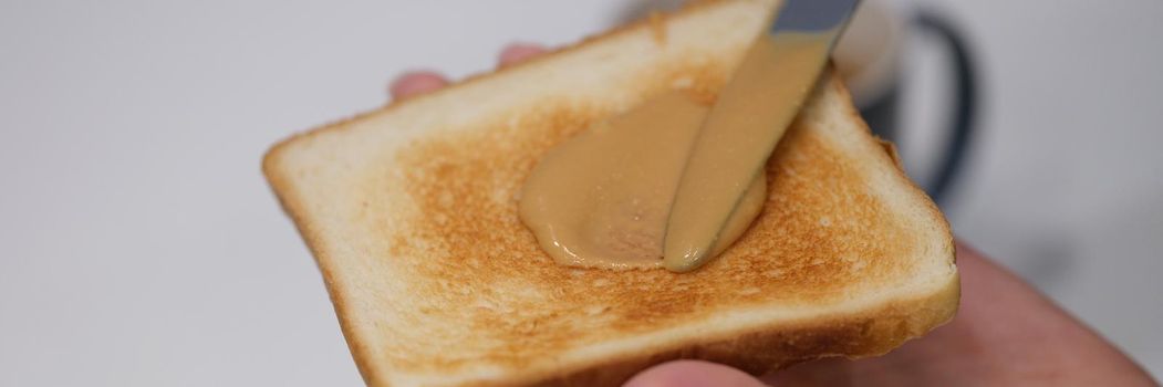 Woman spreads peanut butter on toast with knife. Benefits and harms of peanut butter sandwiches in the morning concept