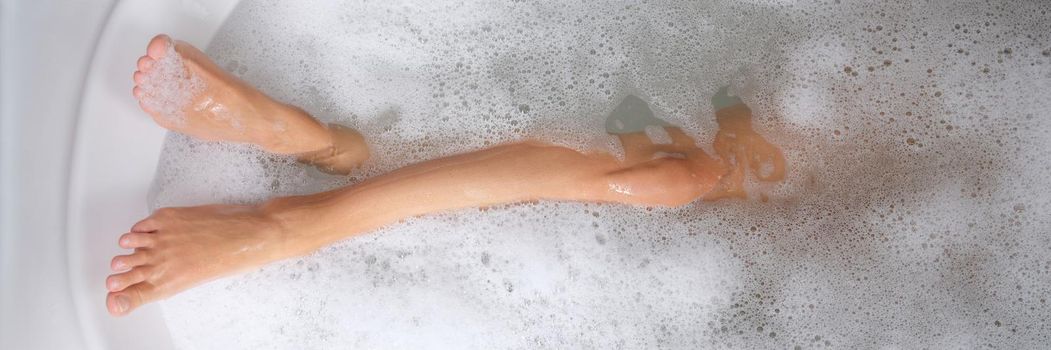 Women beautiful slender legs in bath with water and foam. Benefits and harms of water treatments concept