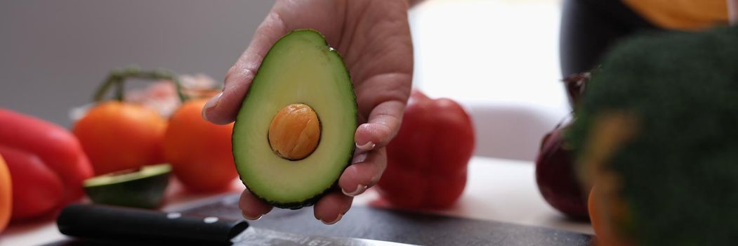 In woman hand cut ripe avocado knife and vegetables lie on table. Benefits of daily avocado consumption concept