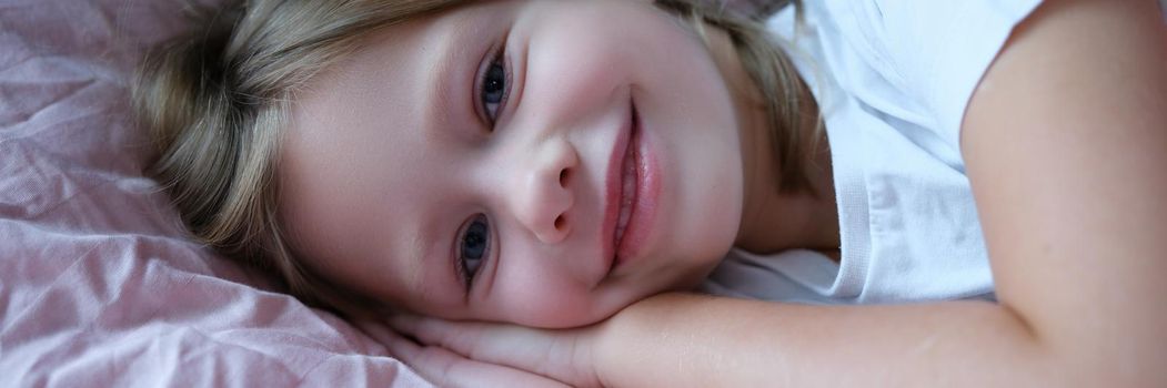 Portrait of little beautiful smiling girl lying on pillow. Baby sleep and healthy sleep rules in children concept