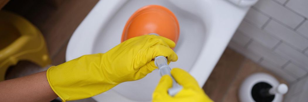 Person in yellow gloves and plunger cleans toilet. Cleanliness and hygiene in toilet concept