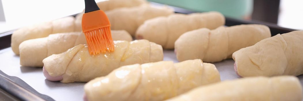 Woman hand is brushing egg yolk onto sweet flour rolls. Cooking croissants at home concept