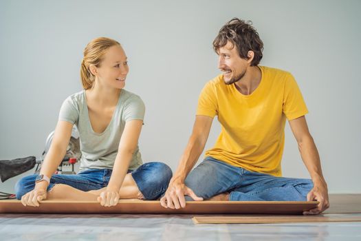 Married couple installing new wooden laminate flooring on a warm film floor. Infrared floor heating system under laminate floor.