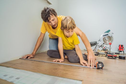 Father and son installing new wooden laminate flooring on a warm film floor. Infrared floor heating system under laminate floor.