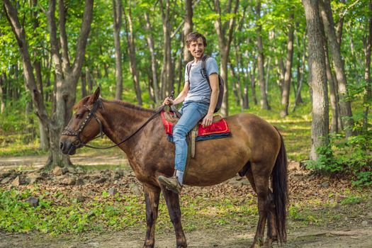 handsome man ride on the black horse in green forest.