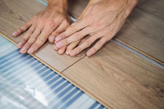 Father and son installing new wooden laminate flooring on a warm film floor. Infrared floor heating system under laminate floor.