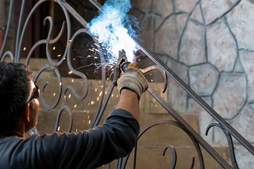 Man in safety glasses is welding metal of staircase. Welding work on metal in private house. Close-up.