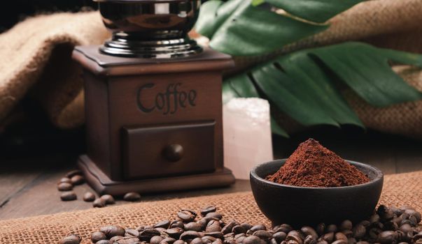 Ground coffee ,roasted coffee beans,grinder,rose quartz stone and monstera leave on wooden table with burlap  background