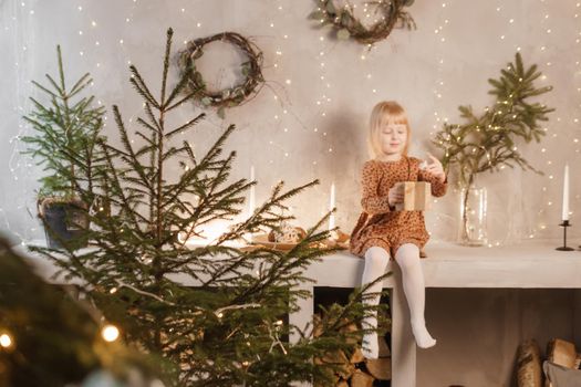 A girl is playing on Christmas Eve in a beautiful house decorated for the New Year holidays. Scandinavian-style interior with live fir trees and a wooden staircase.