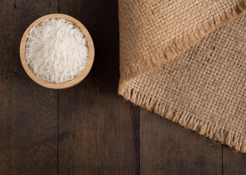 Jasmine  rice in wooden bowl on  Sackcloth,burlap hessian  table background  with copy space,top view