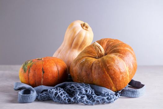 Close-up three fresh ripe pumpkins in environmentally friendly reusable mesh bag made from recycled materials on gray background. Healthy food concept, vegetarianism, no plastic. Selective focus.